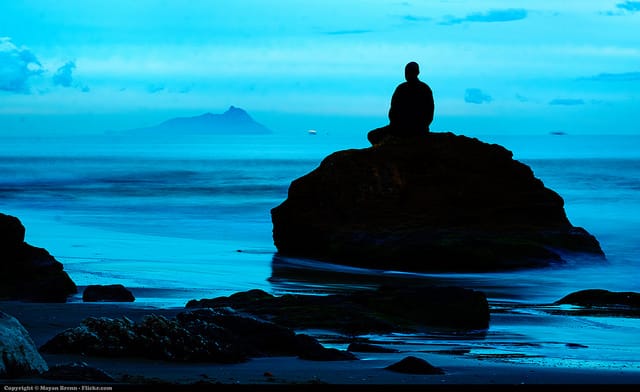 A monk sitting on a rock in the ocean in meditation.