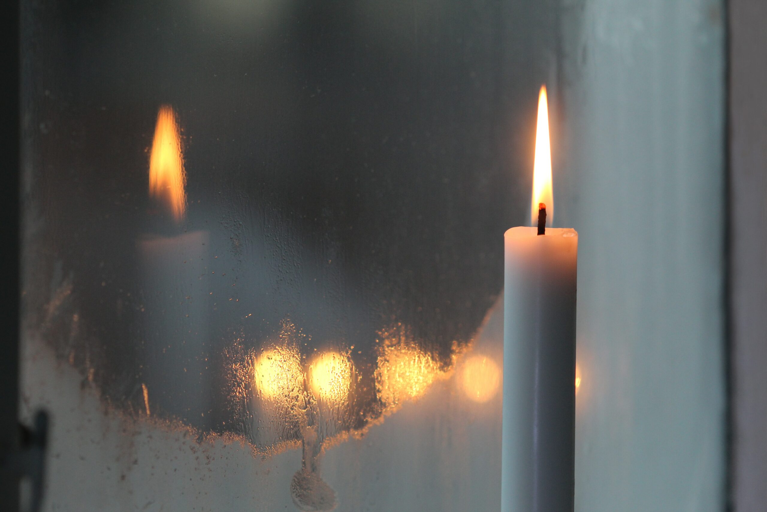 a white candle reflects on a frosted window