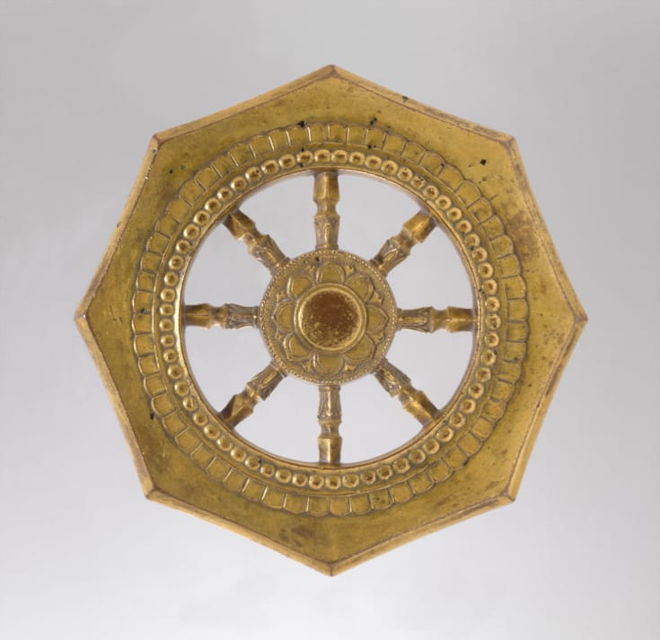 Wheel of Dharma. A bronze wheel with eight spokes and a lotus flower at its center.