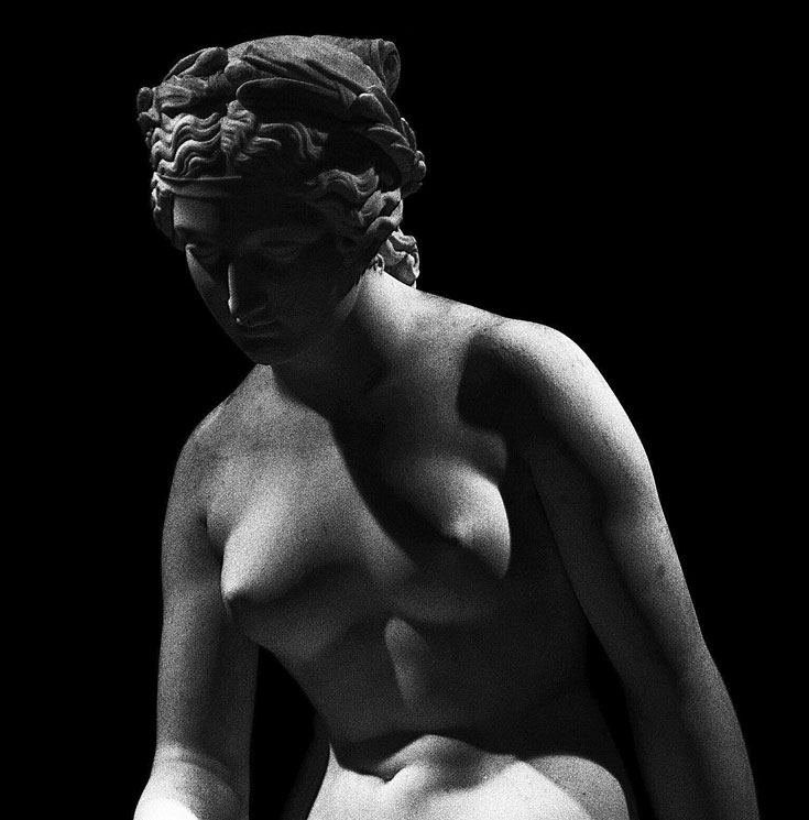 A black and white photo of a marble sculpture of a naked woman from the waist up.